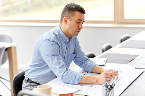 Архитектор-перфекционист сидит за столом и проверяет чертеж