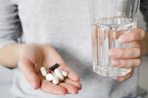 Девушка с нозофилией держит в руках таблетки и стакан с водой