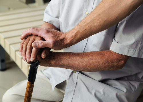 Мужчина положил руку на руки сидящего пожилого мужчины с болезнью Паркинсона